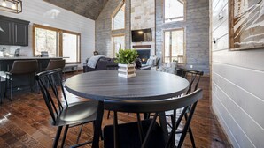 A spacious living area with a round table, chairs, a fireplace, and a television mounted on the wall. - Sunrise Retreat - Hot Tub, 2 Story Deck, Pet Friendly, Free Firewood (Broken Bow)