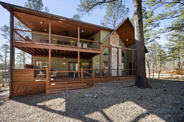 A two-story log cabin with a balcony, large windows, and a stone fireplace.