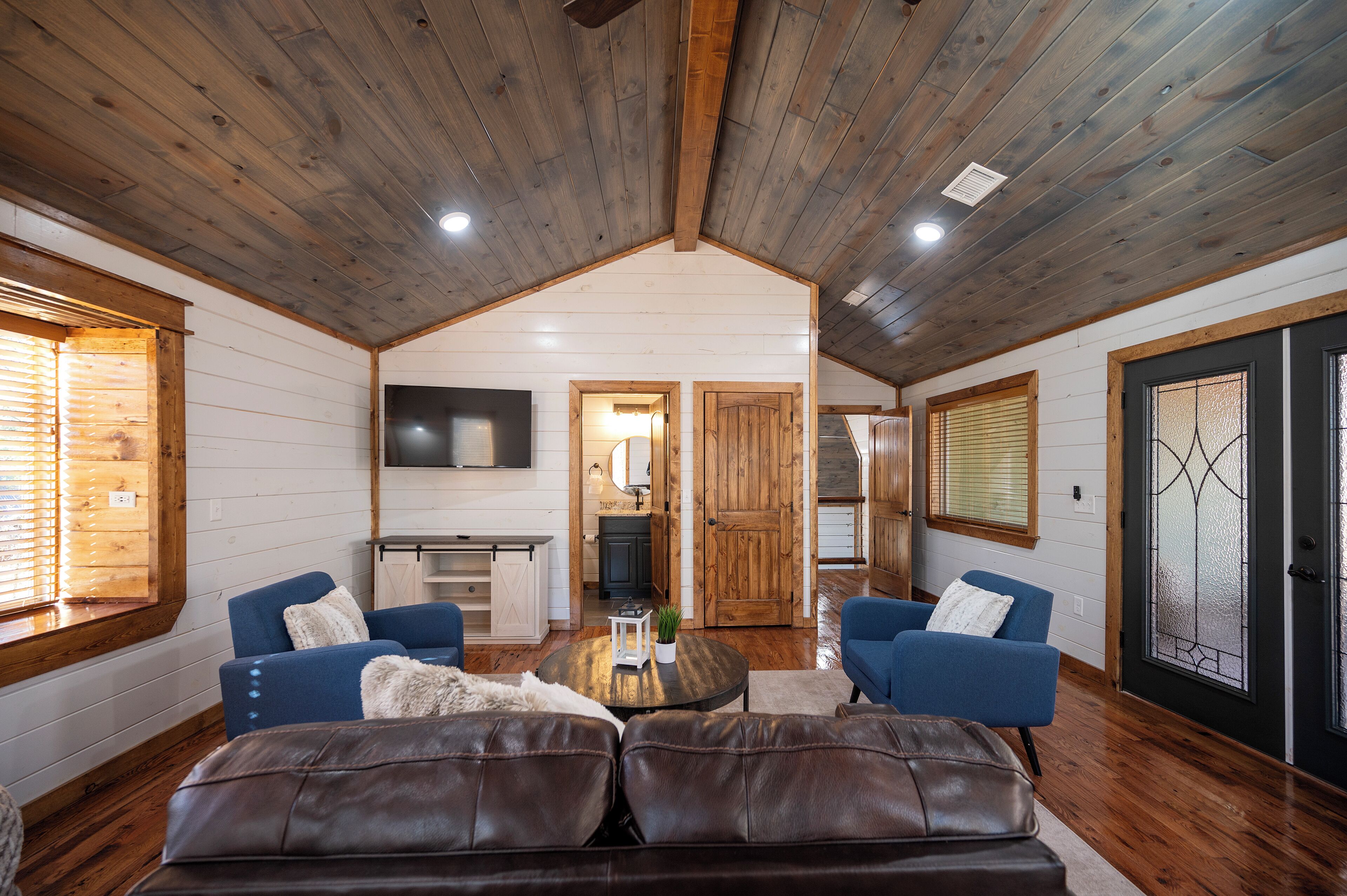 A spacious living area with a high ceiling, wooden walls, a central coffee table, blue sofas, and a leather couch.