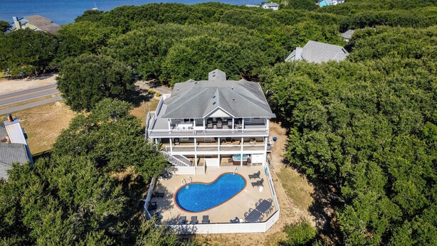 A large house with a swimming pool surrounded by dense trees, overlooking a body of water. - Z's By The Sea: Private Pool | Hot Tub | Rec Room (Kitty Hawk)