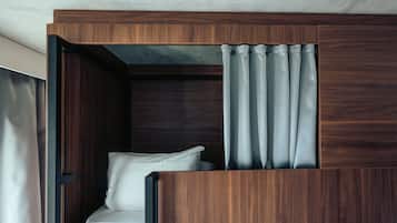 Quarto moderno e compacto com cabeceira de madeira, uma cama de solteiro e uma cortina parcialmente fechada.