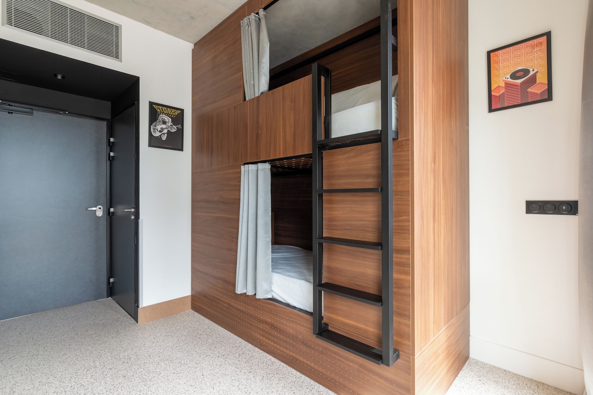 Una habitación con literas, una puerta, un cuadro enmarcado y un interruptor de luz en la pared.