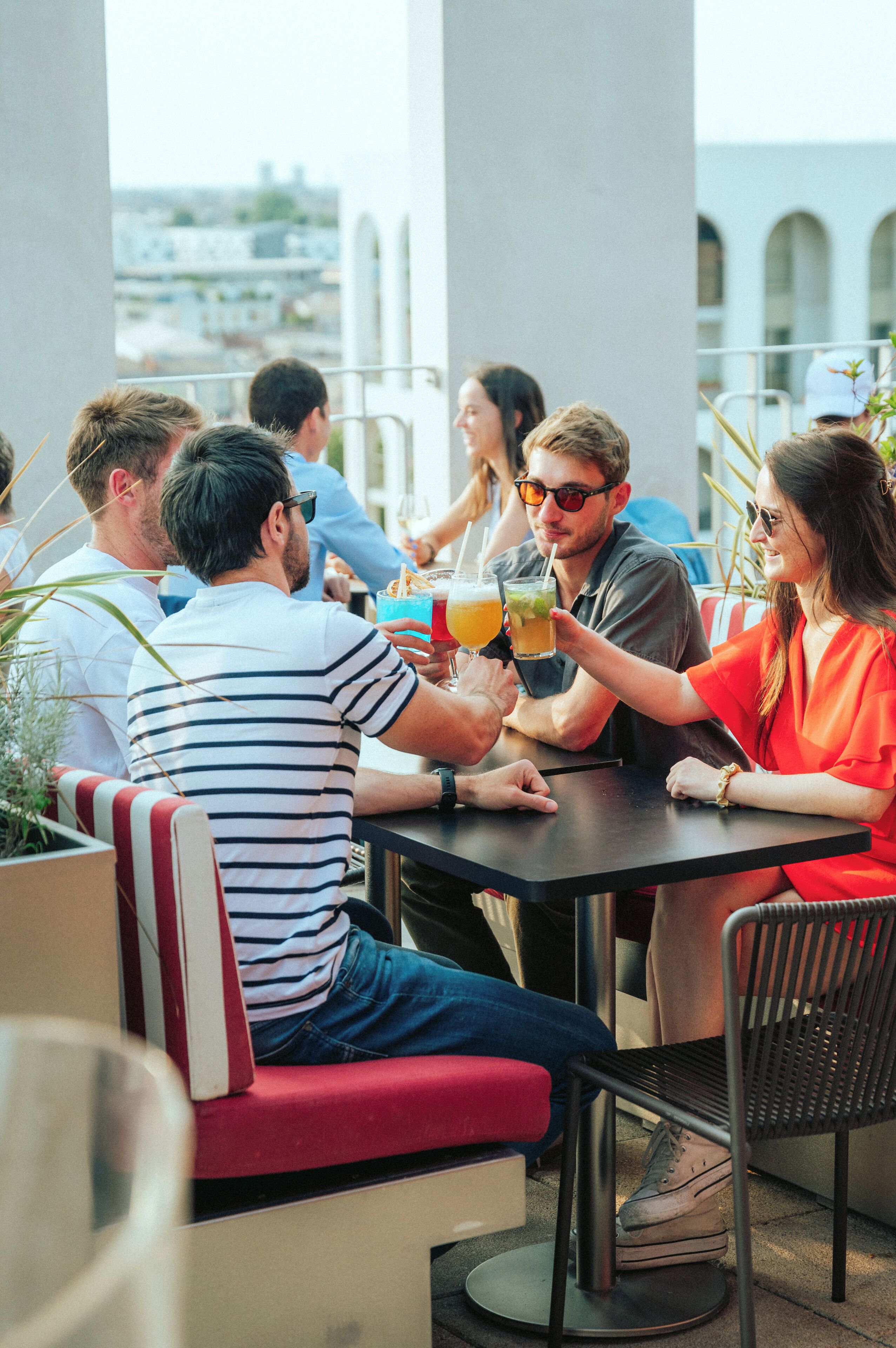 Un grupo de personas sentadas en una mesa al aire libre con bebidas, en un entorno con vistas a edificios al fondo.