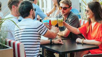 Un grupo de personas sentadas en una mesa al aire libre con bebidas, en un entorno con vistas a edificios al fondo.