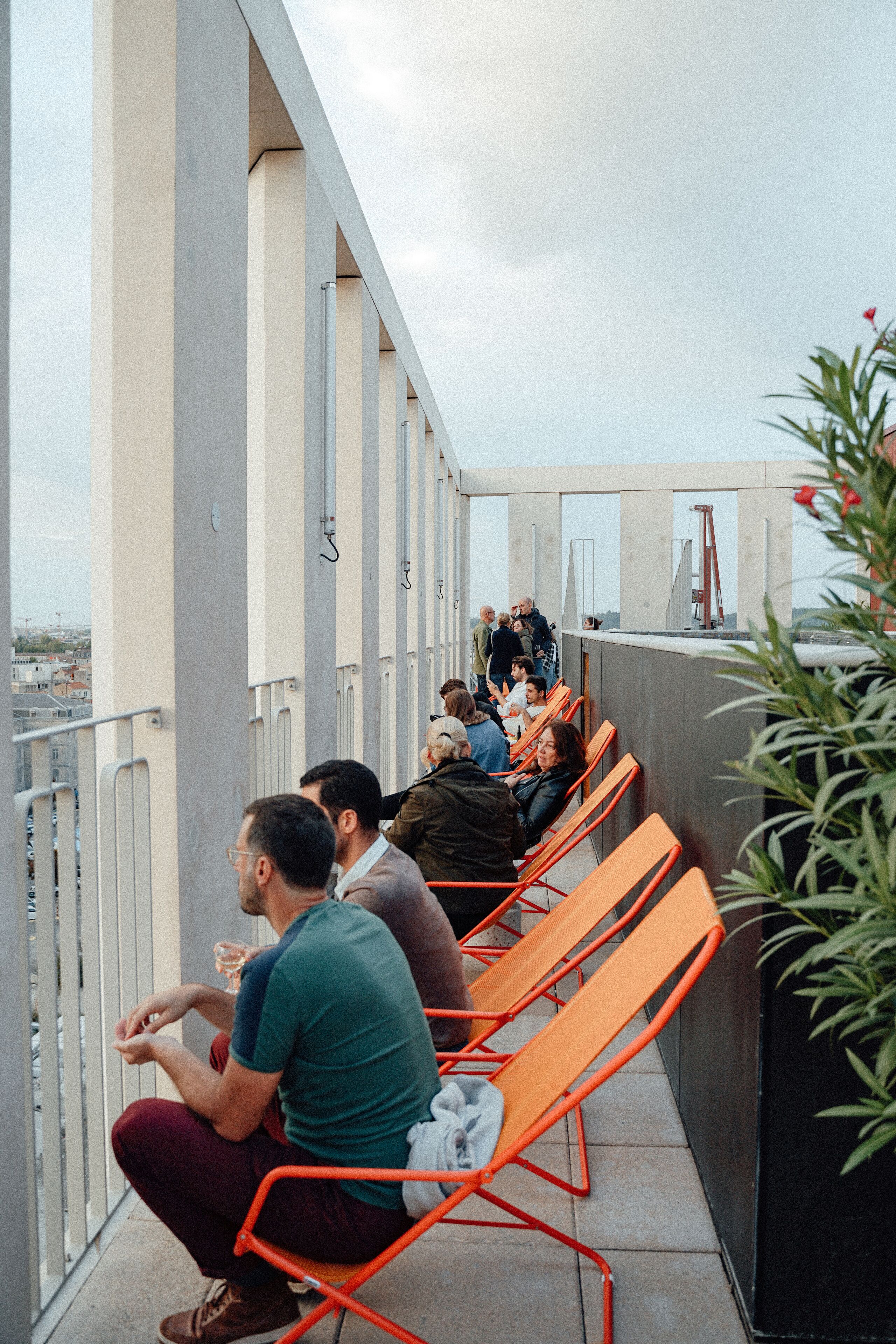 Een balkon met oranje stoelen en een hekwerk, met uitzicht op een stadsbeeld.