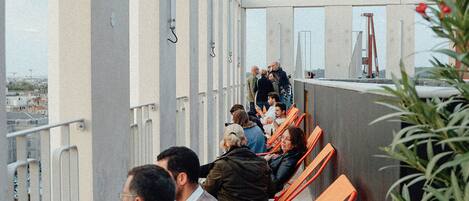 Een balkon met oranje stoelen en een hekwerk, met uitzicht op een stadsbeeld.