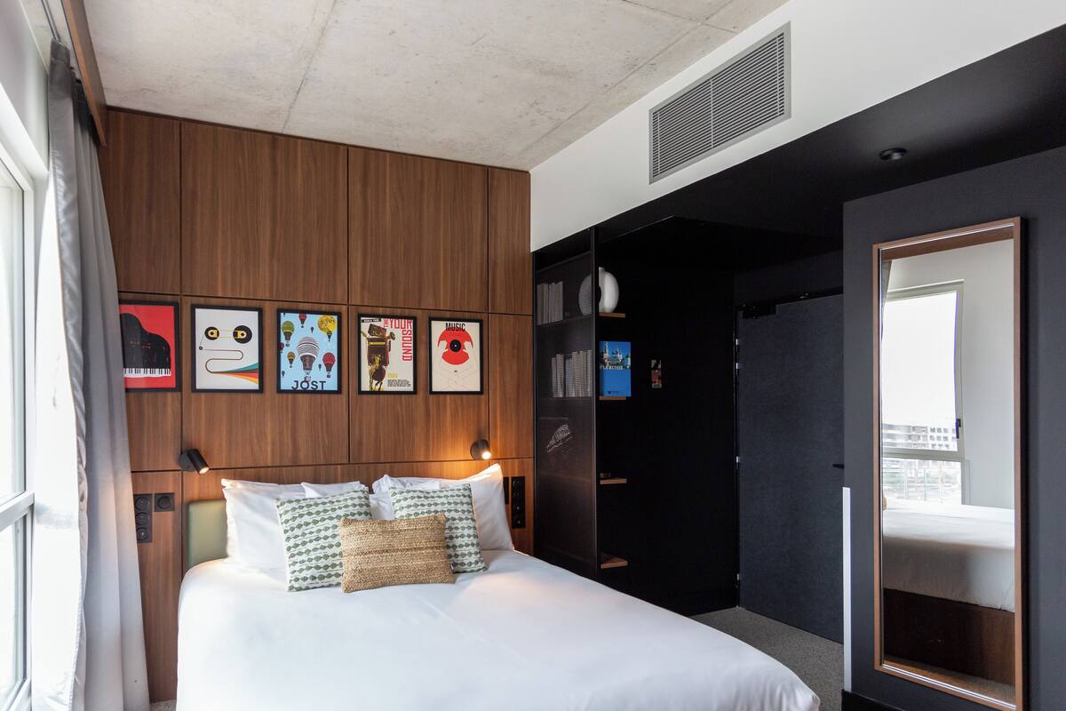 Une chambre d’hôtel moderne avec un grand lit, des murs recouverts de panneaux en bois et des œuvres d’art encadrées accrochées au mur.