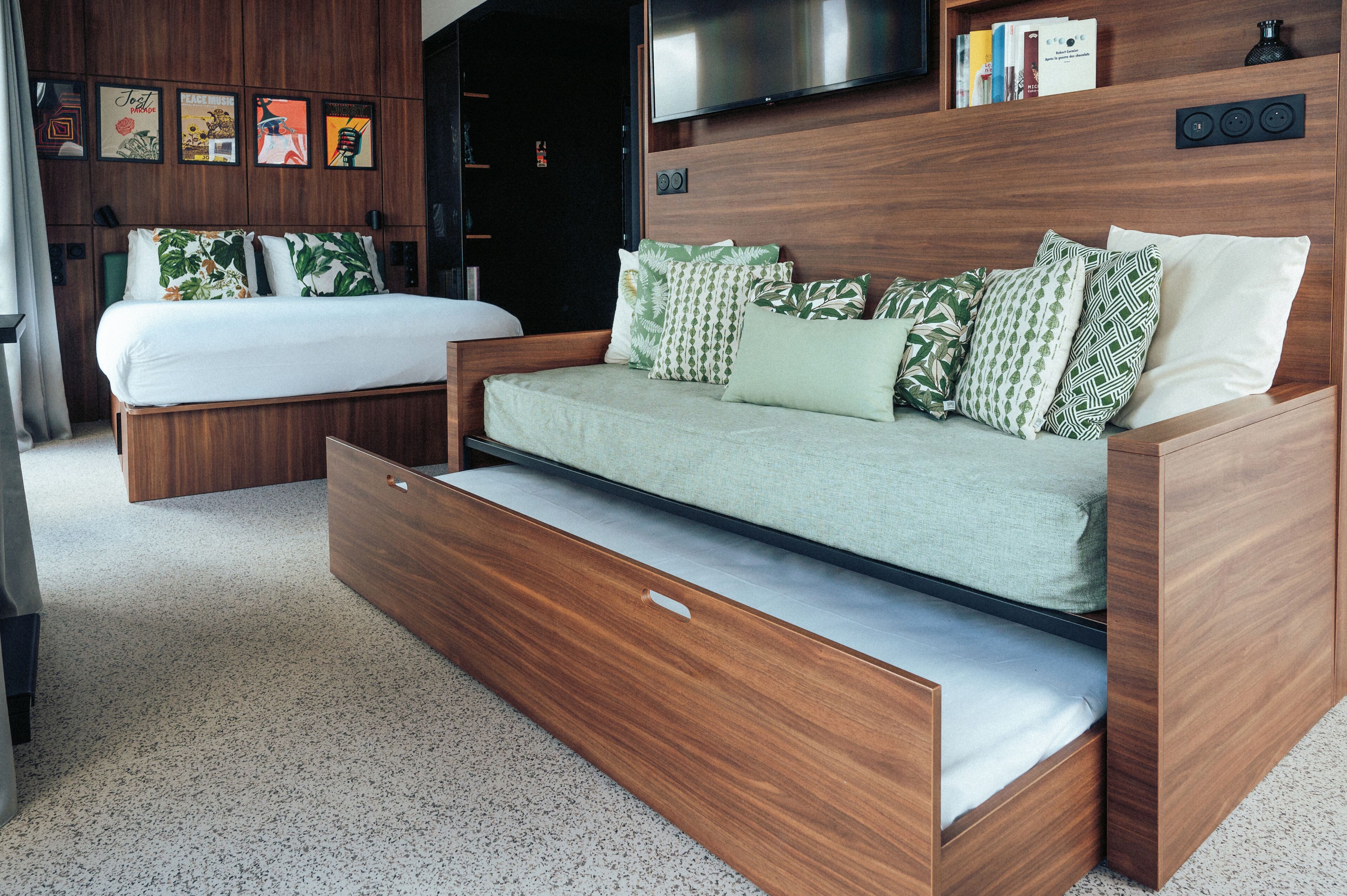 Un dormitorio moderno con una cama, un sofá cama y un televisor montado en la pared.