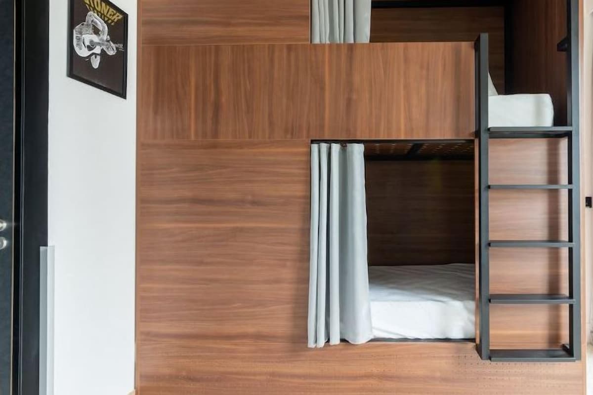 Una litera con escalera, paneles de madera y una ventana con cortinas.