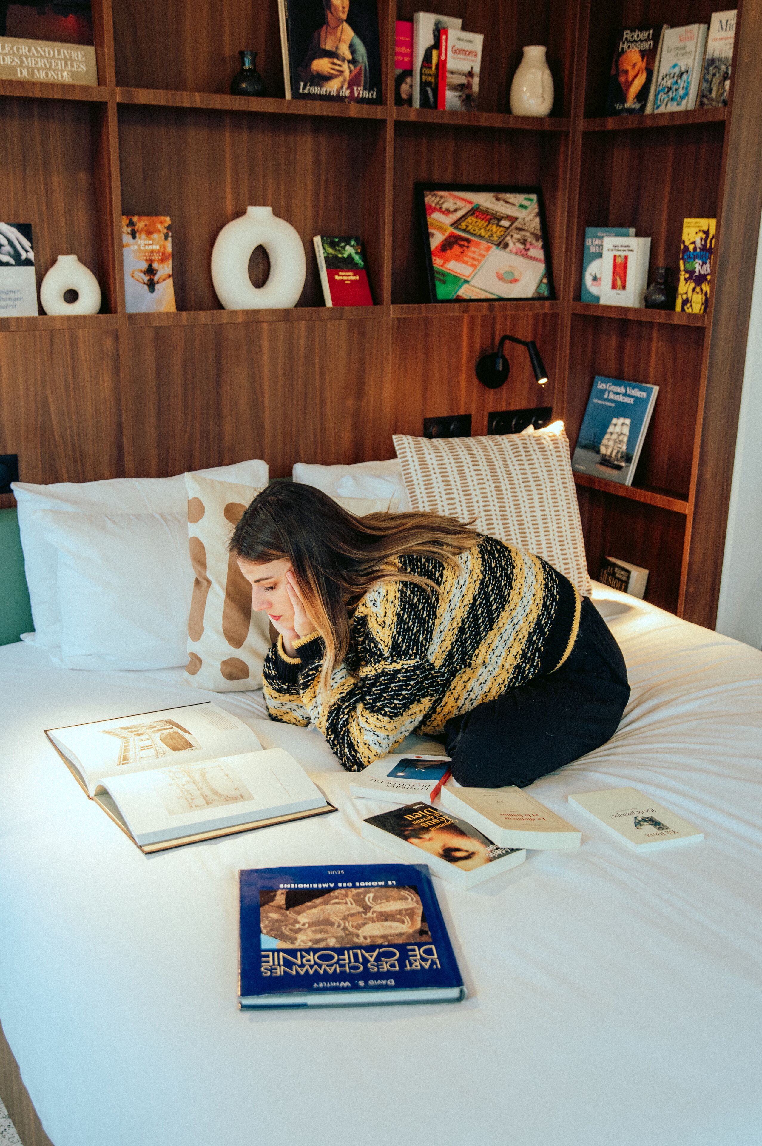 Eine Person liegt auf einem Bett mit Büchern und einer Lampe.
