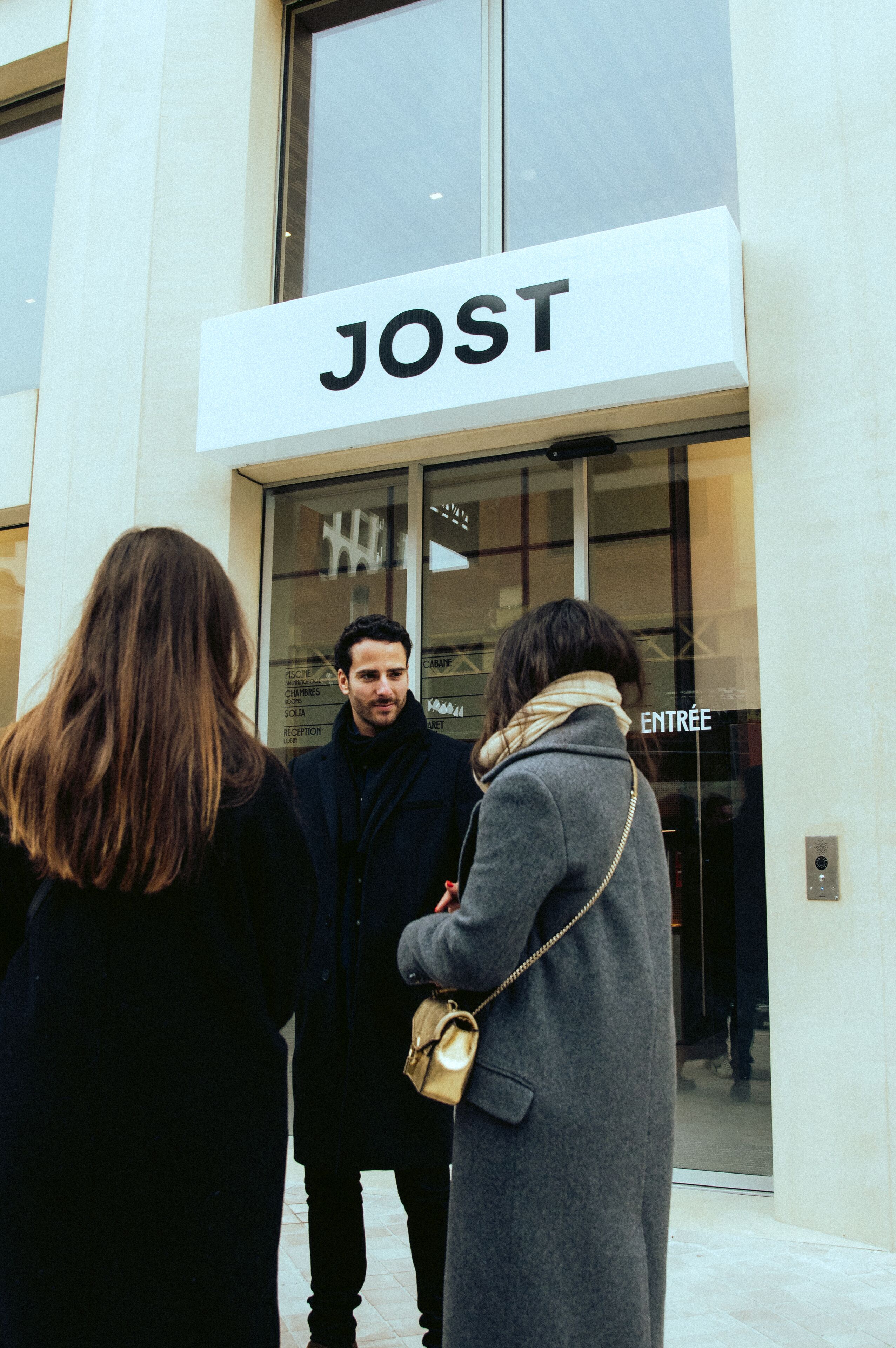 A group of people standing outside a building with a sign that reads "JOST".