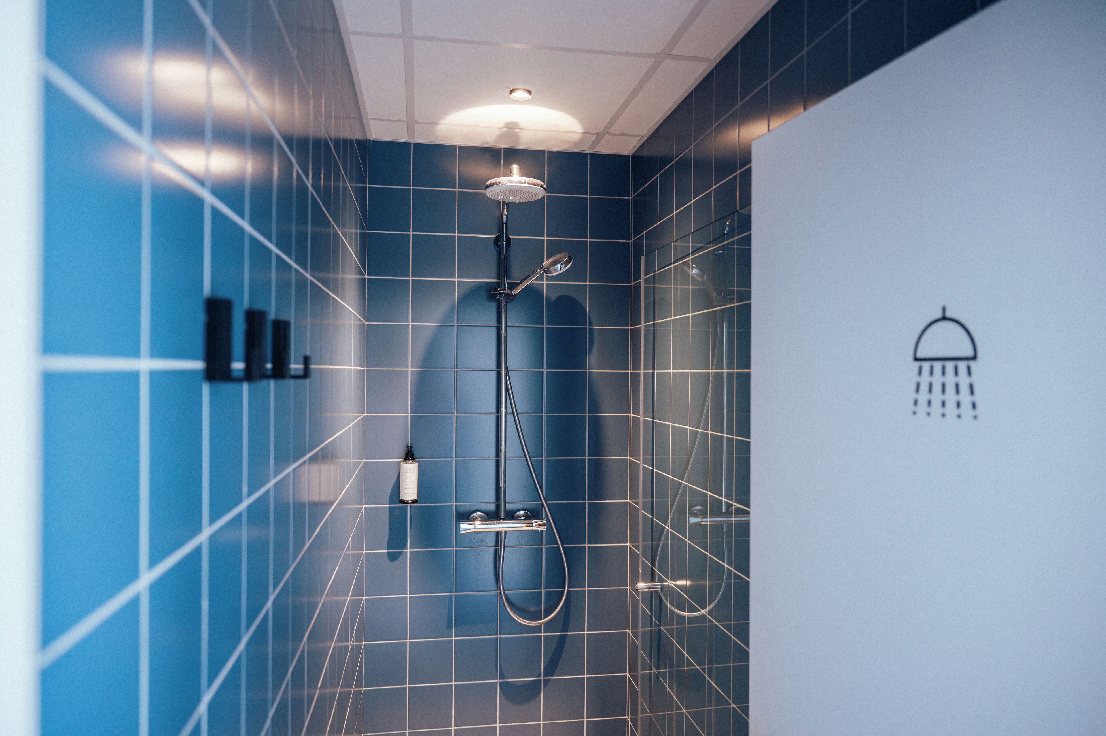 Un baño moderno con azulejos azules, cabezal de ducha y secamanos.