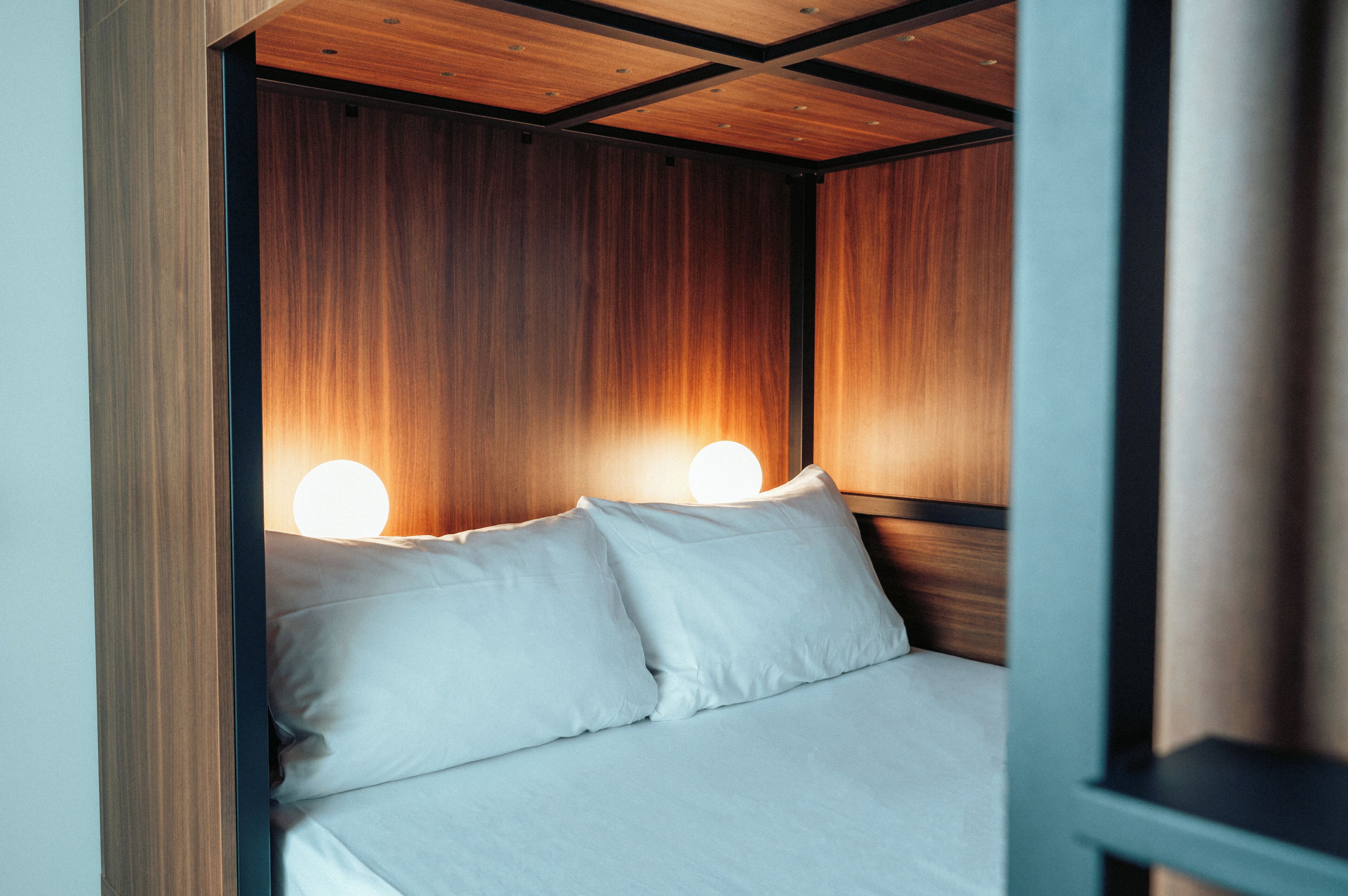 Een net opgemaakt bed met witte lakens en twee ronde wandlampen.