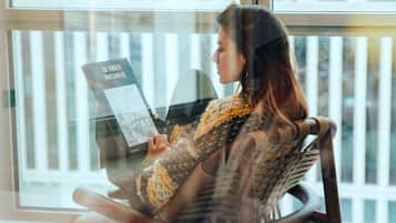 Una persona sentada en una mecedora junto a una ventana, leyendo un libro.