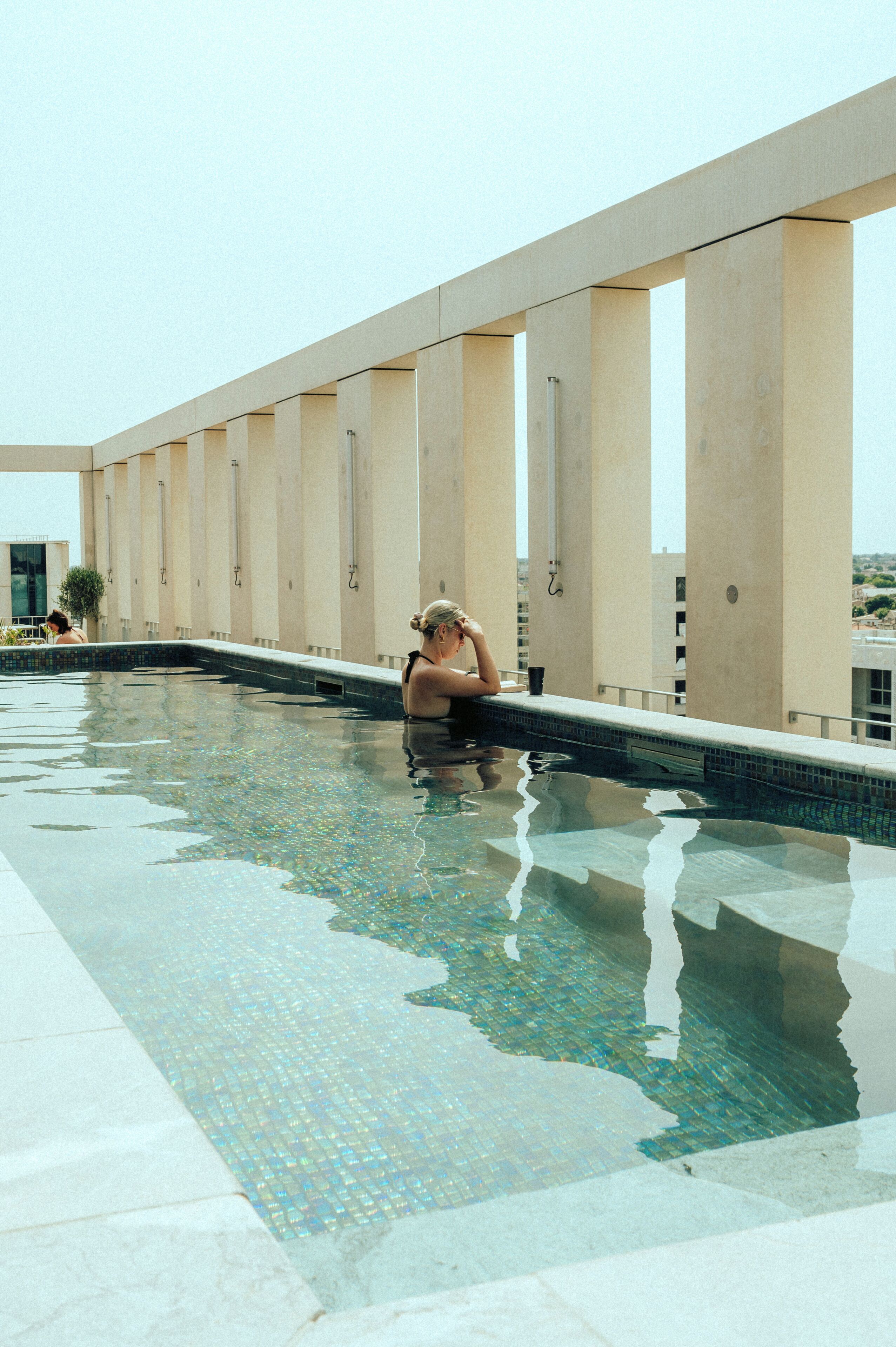 Une piscine dont le fond est carrelé, avec une personne assise au bord.