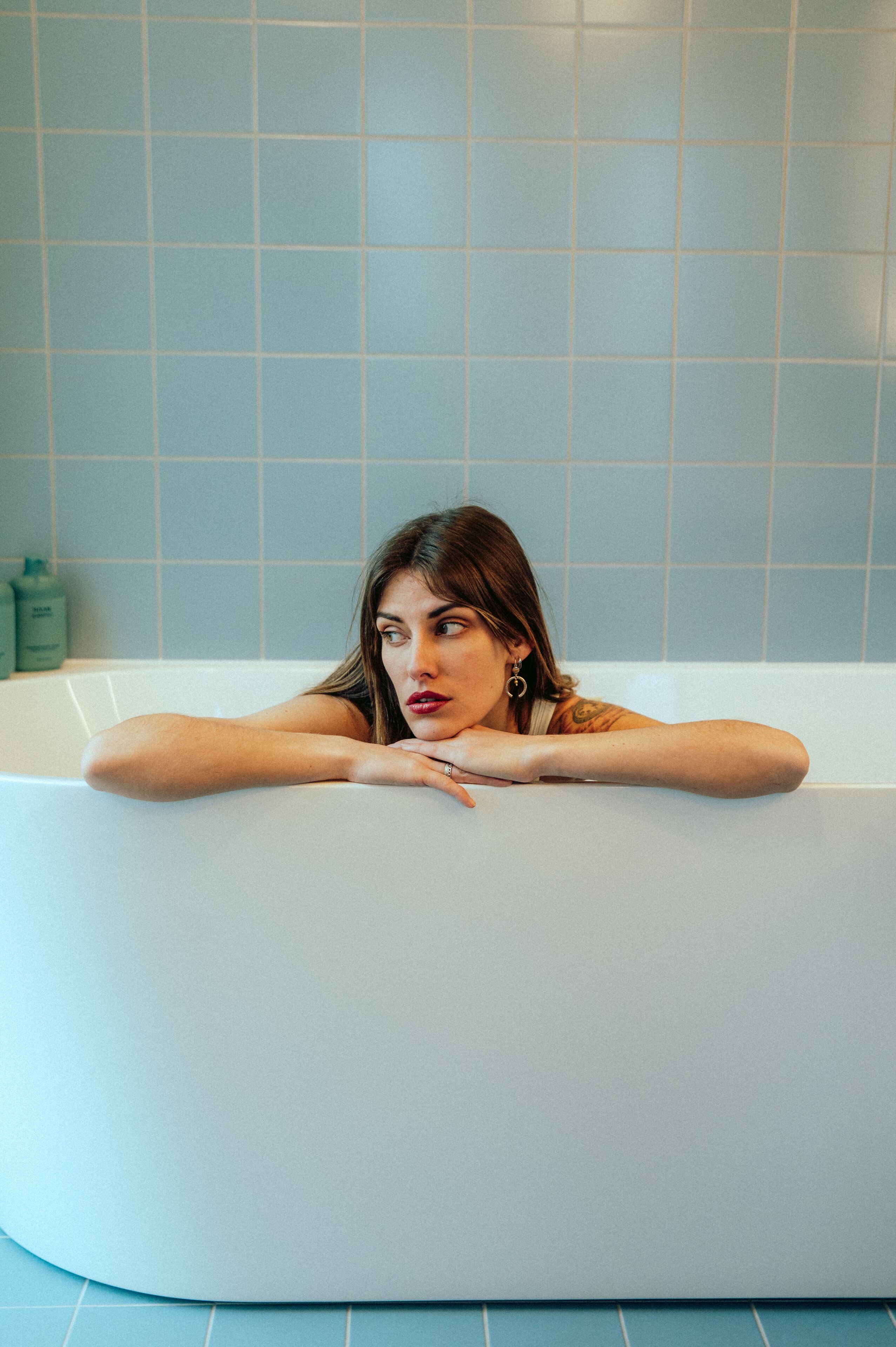 Una persona appoggiata a una vasca da bagno in un bagno con piastrelle blu.