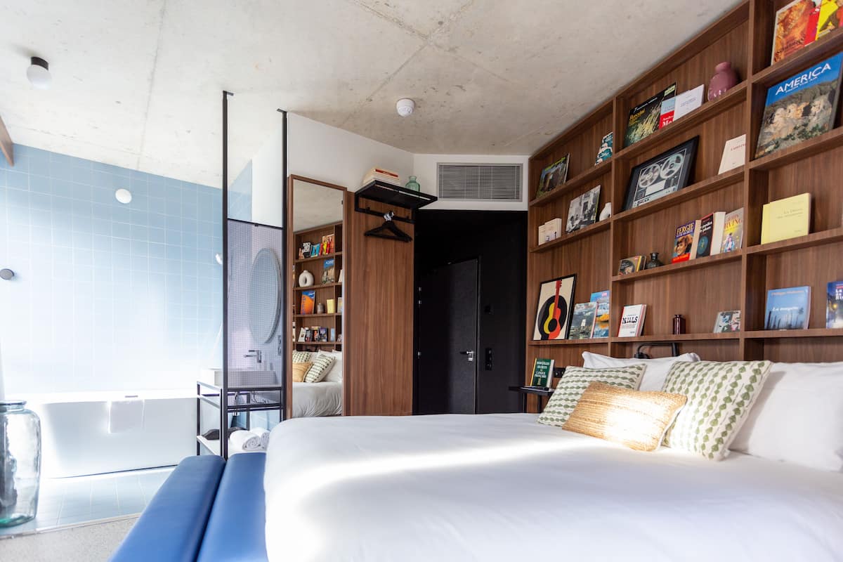 Une chambre moderne avec un grand lit, une bibliothèque intégrée, un espace douche et une vue sur l’extérieur.