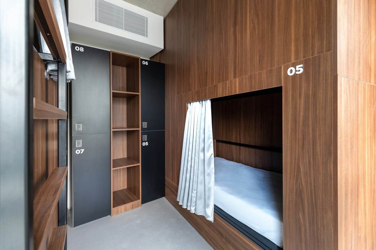 Habitación moderna y compacta con literas identificada con el número '05', armarios empotrados numerados '06' y '07', y un ventanal con cortina.
