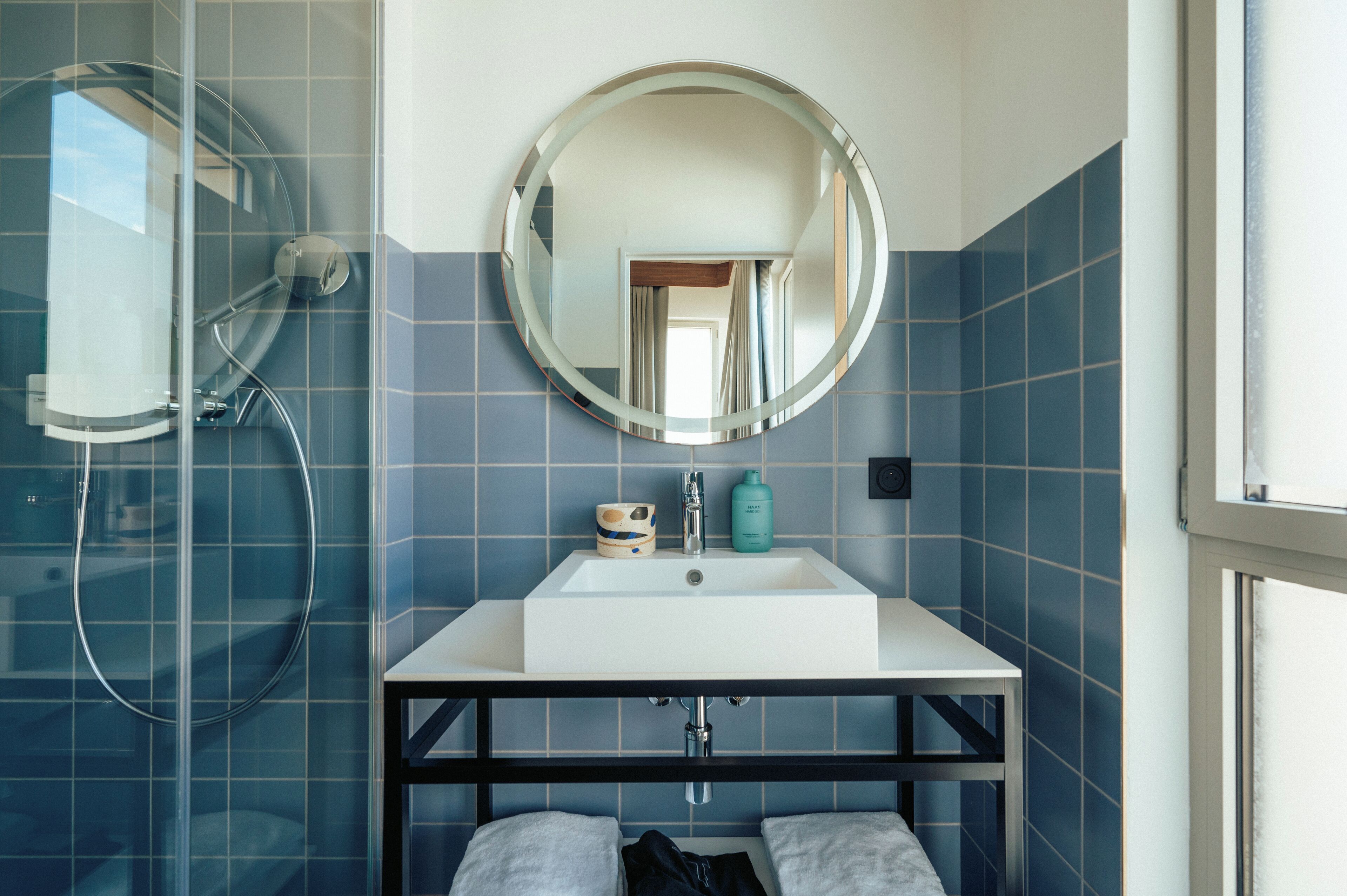 Une salle de bain avec une douche à parois de verre, un lavabo blanc avec un miroir au-dessus, et des murs recouverts de carreaux bleus.