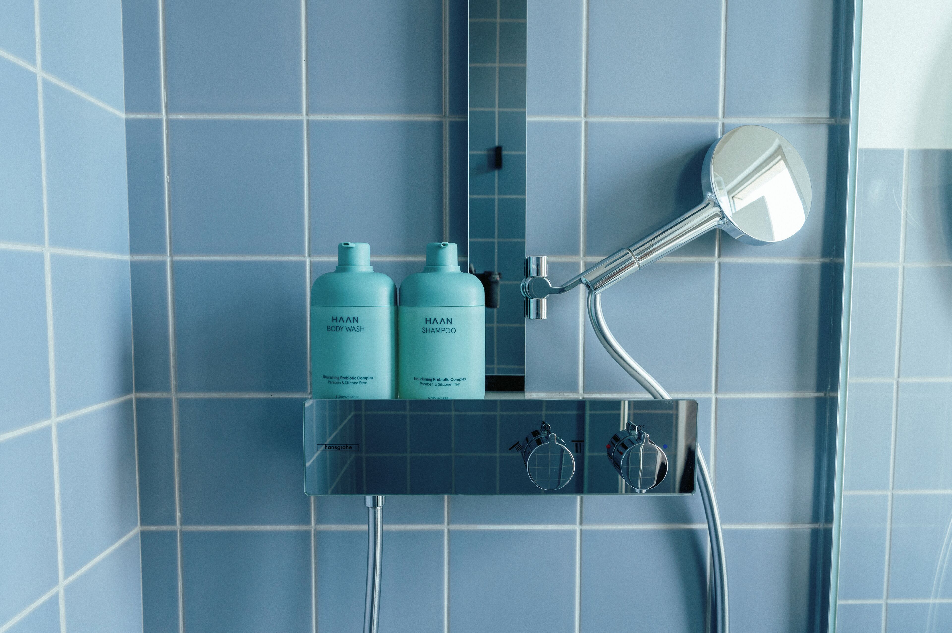 A bathroom with a shower, two bottles of Haan body wash, and a mirror.