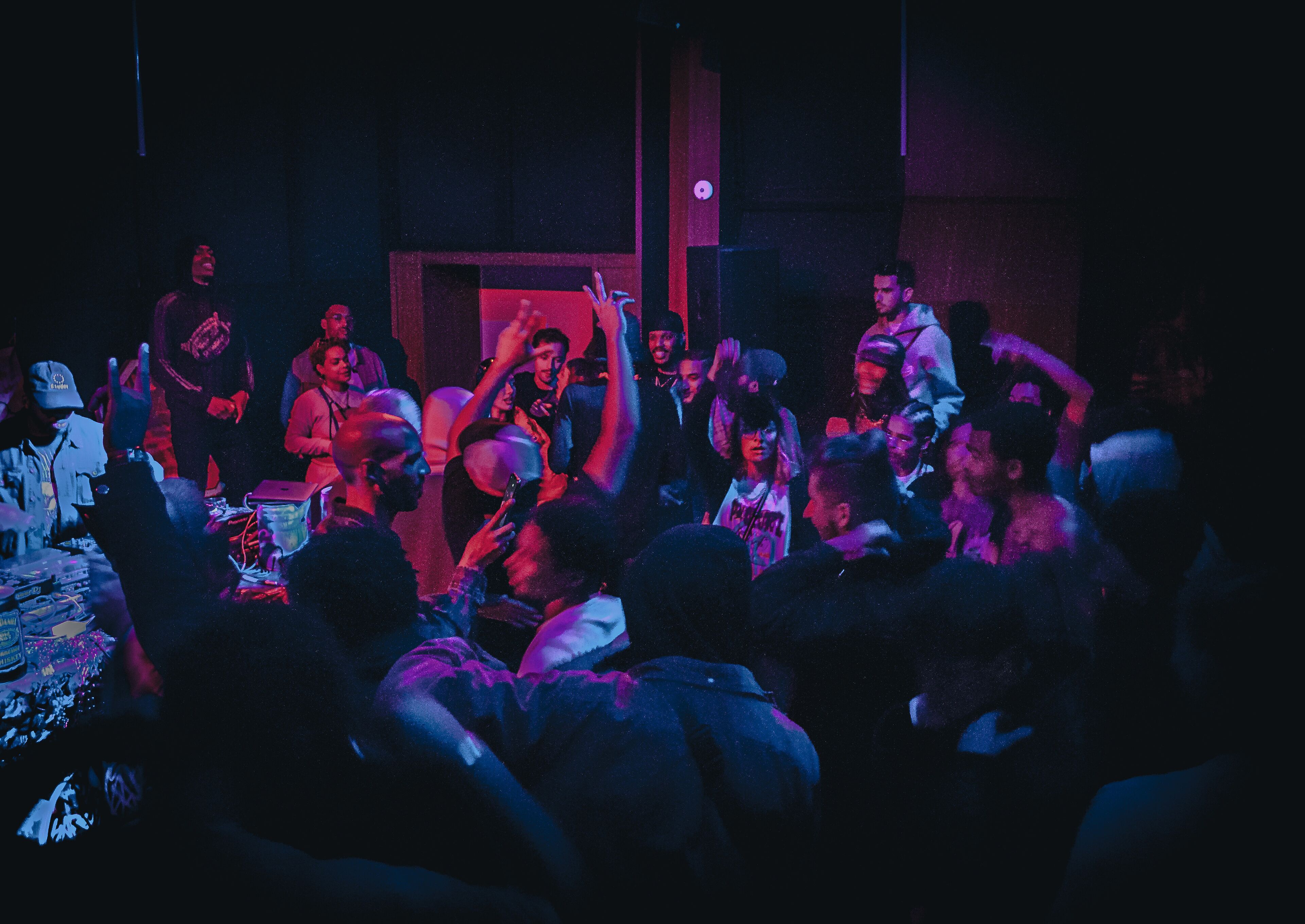 A crowded indoor event with people standing and sitting, some holding up phones.