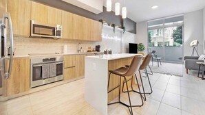 A modern kitchen with wooden cabinets, a built-in microwave, and a central island with bar stools. - Brand New Cool 1 Bdrm Condo In Best Miami Location (Miami)