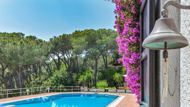 A swimming pool with a tiled deck, surrounded by lush greenery and trees. - Villa Ottagonale, Capo Perla (Capoliveri)