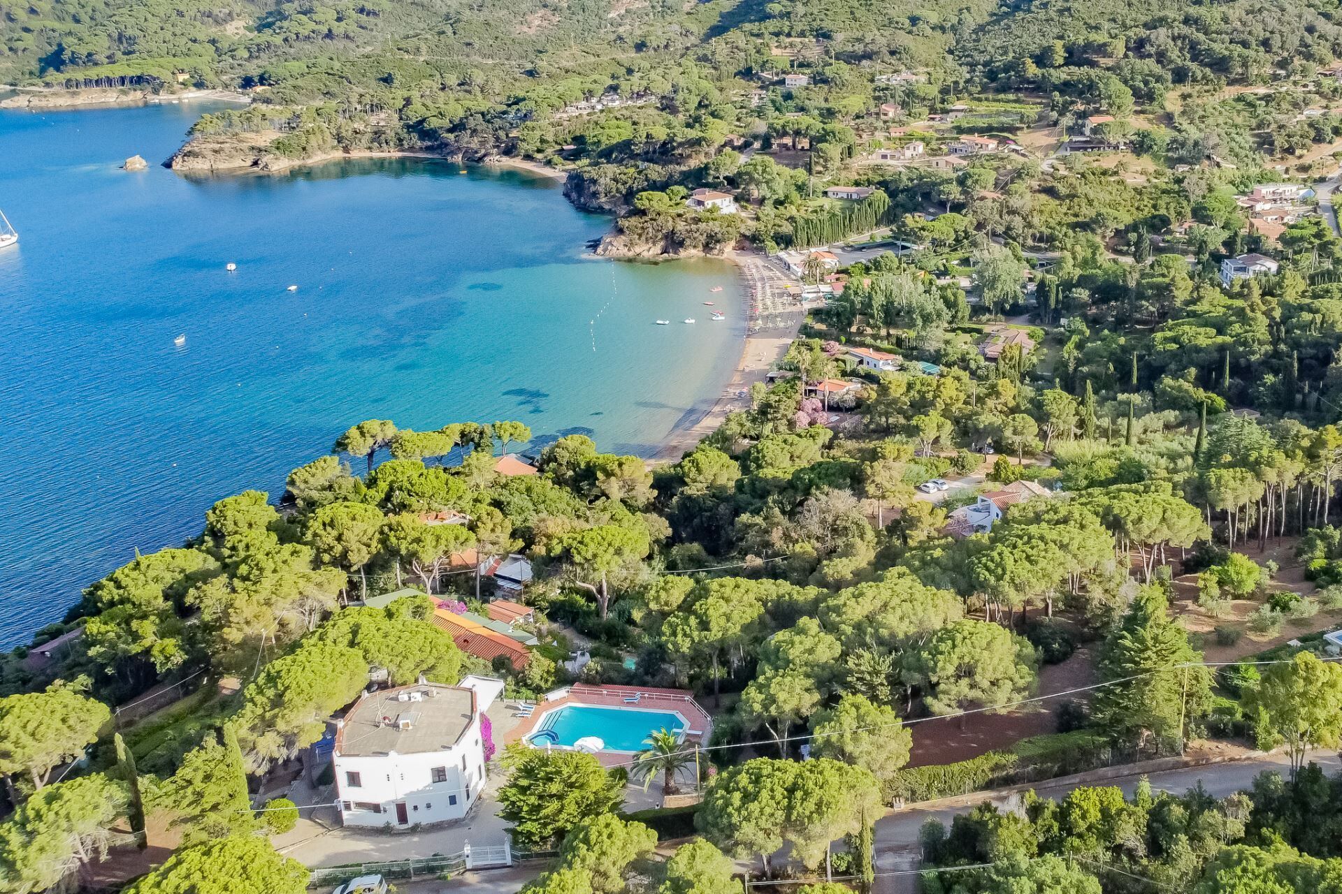Vista aerea di una proprietà costiera con piscina, circondata da vegetazione lussureggiante e una spiaggia.