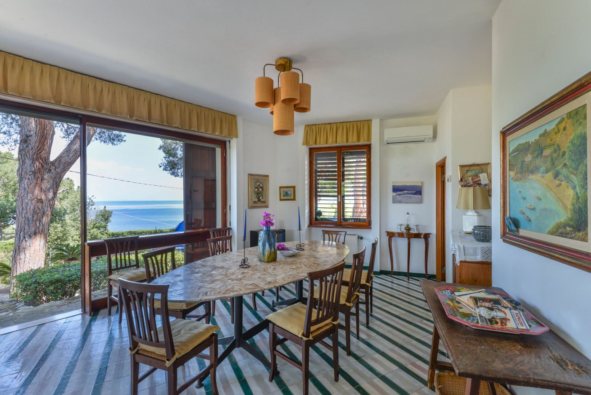 Un espace repas avec une table ronde, des chaises et une vue sur la mer grâce à de grandes fenêtres.