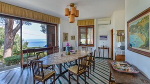 A dining area with a round table, chairs, and a view of the sea through large windows. - Villa Ottagonale, Capo Perla (Capoliveri)
