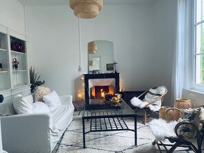 Un salon chaleureux avec une cheminée, des meubles blancs et une table basse en verre.
