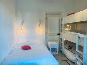 Une chambre avec un lit simple, une petite table de chevet, une armoire blanche et un lit superposé agrémenté d’une lumière décorative.