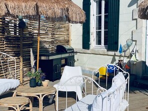 Un espace extérieur aménagé avec des meubles en osier, un barbecue et un parasol en chaume.