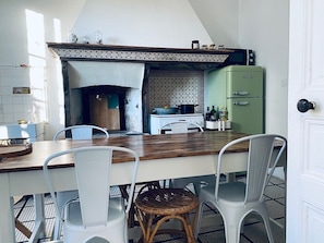 A kitchen with a central island, white chairs, a wicker chair, a green refrigerator, and a tiled backsplash.