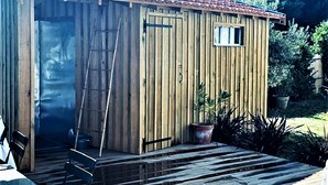 Un cobertizo de madera con techo de tejas, una escalera apoyada en él y un ventanal pequeño.
