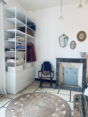Una stanza con un armadio bianco, una sedia, un camino e un tappeto intrecciato.