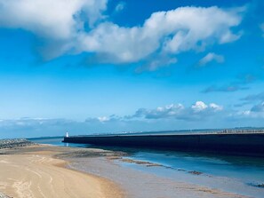 A coastal scene with a sandy beach, a pier extending into the water, and a lighthouse in the distance.