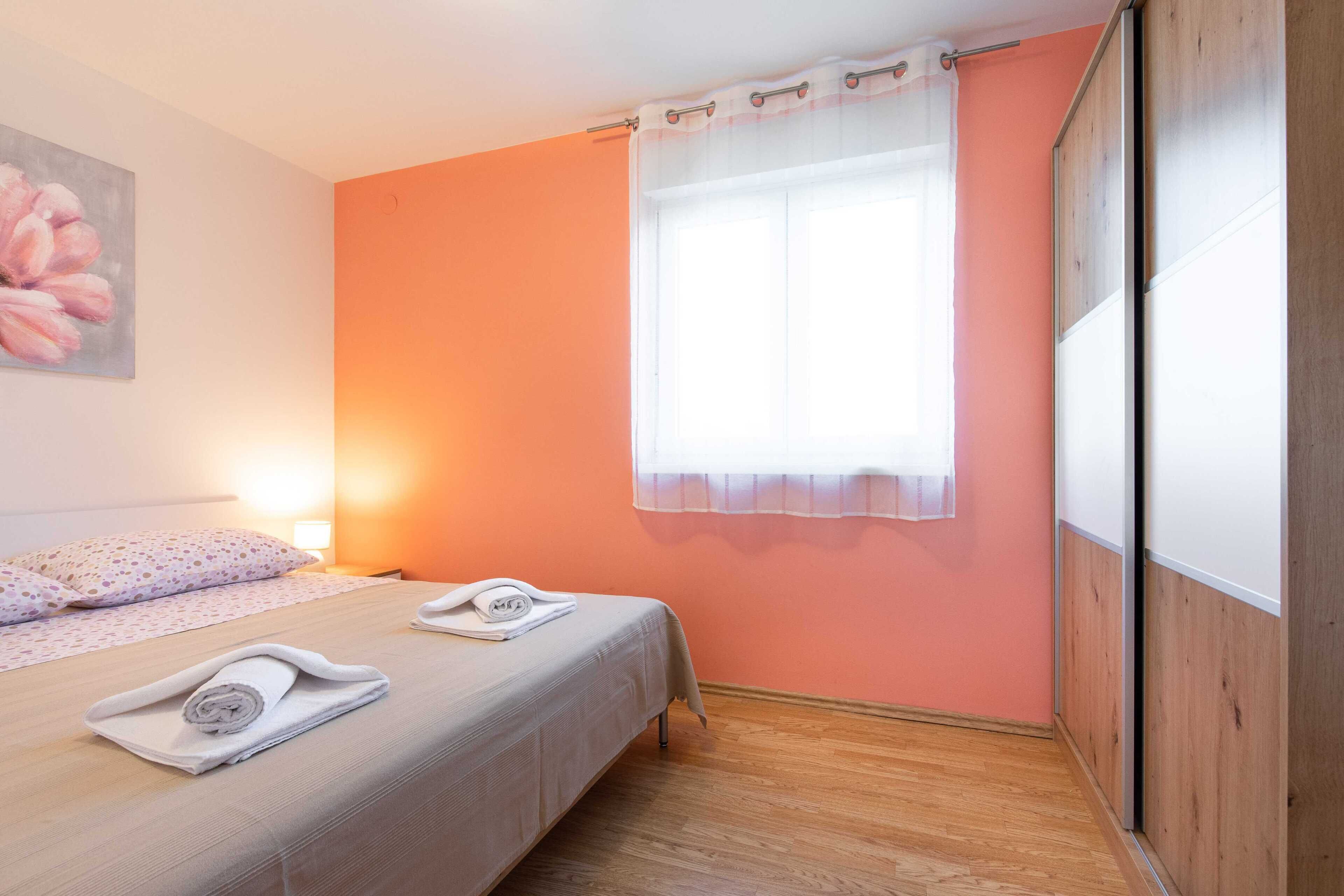 Une chambre d’hôtel avec un lit, une fenêtre ornée de rideaux légers, un tableau au mur et un plancher en bois.