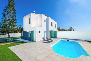 Une maison moderne à deux étages, dotée d’une piscine, de volets verts et d’une pelouse bien entretenue.