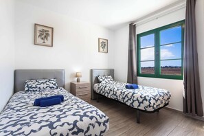 Un dormitorio con dos camas, una mesita de noche, una lámpara y una ventana con cortinas.