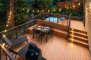 A wooden deck with a hot tub, outdoor dining area, and string lights.
