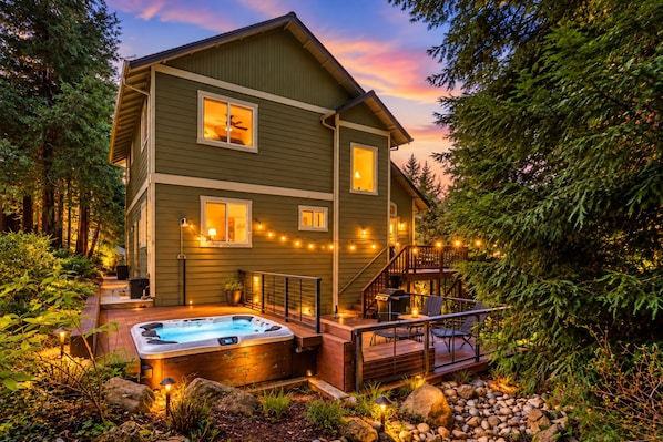A two-story house with a hot tub, deck, and string lights.
