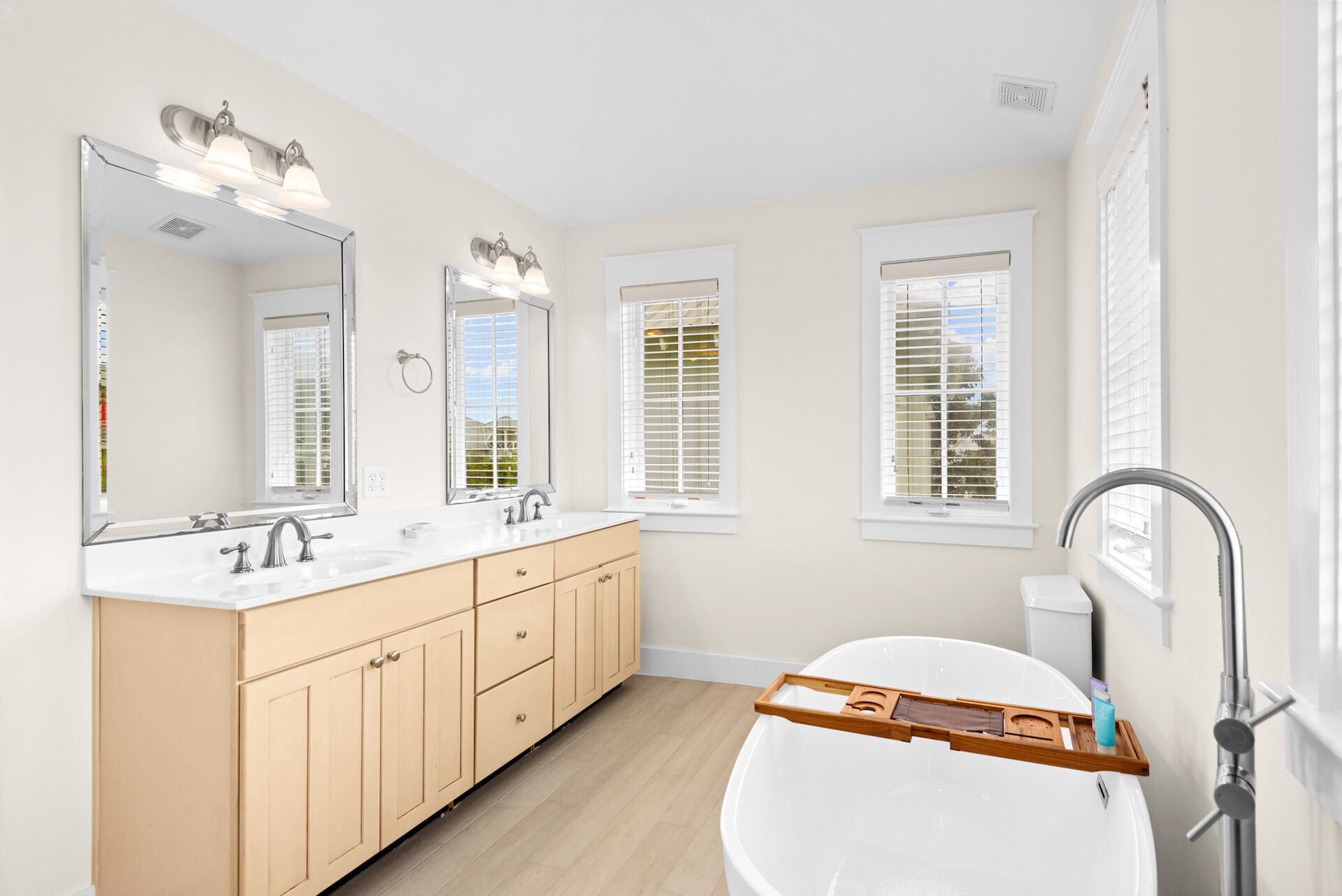 A modern bathroom with a double sink vanity, a large mirror, and a bathtub with a wooden tray.