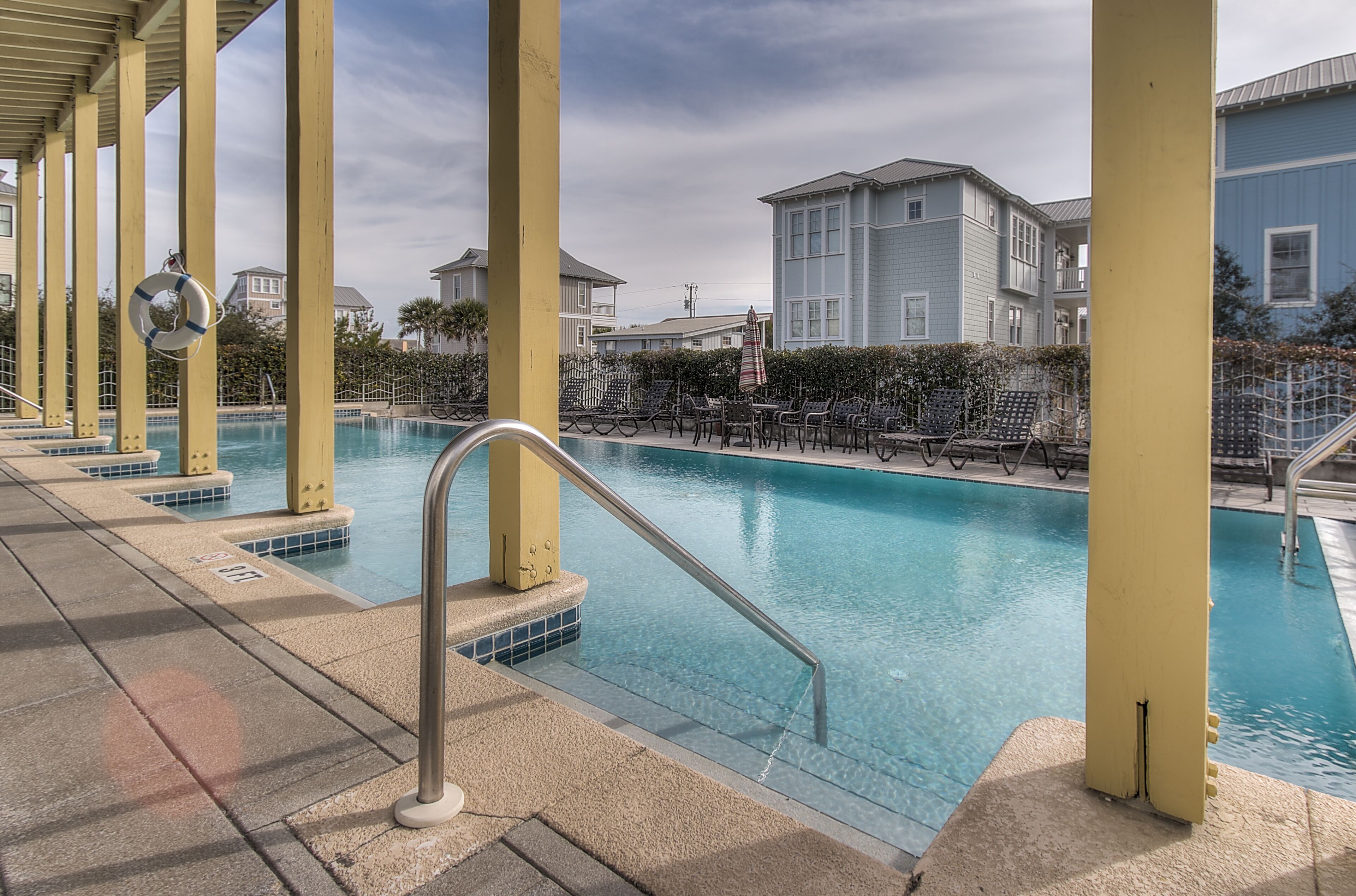 A pool area with a clear view of the pool, a lifebuoy, and a chair with an umbrella.
