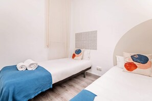 A hotel room with two single beds, a window with curtains, a tiled wall, and a wooden floor.
