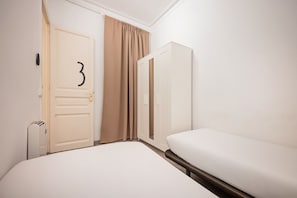 Ein Hotelzimmer mit einem Einzelbett, einem Kleiderschrank, einer Tür mit der Nummer 3 und einem Fenster mit Vorhängen.
