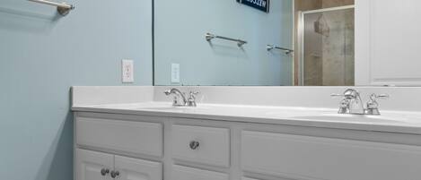 A bathroom with a white vanity, two sinks, a towel rack, and a welcome sign.