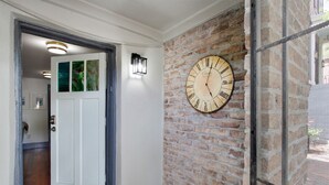A hallway with a brick wall, a large clock, and a door leading to another room. - Ground Level Apartment in City Center by Perry Lane Hotel (Savannah)