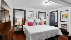 A neatly arranged bedroom with a large bed, two bedside tables with lamps, a wooden dresser, and a door leading to another room. - Ground Level Apartment in City Center by Perry Lane Hotel (Savannah)