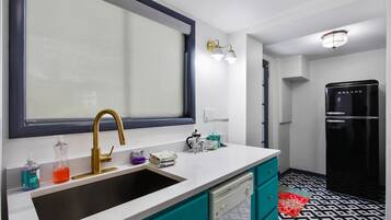 Una cocina moderna con un ventanal grande, un grifo dorado, armarios color turquesa y un refrigerador negro.